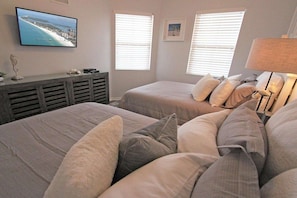 Ein Schlafzimmer mit zwei Betten, einem an der Wand befestigten Fernseher und einem Fenster mit Jalousien.