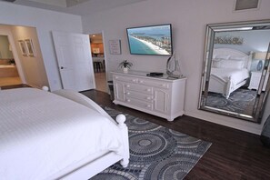 A bedroom with a large bed, a dresser, a mirror, and a television displaying a beach scene.