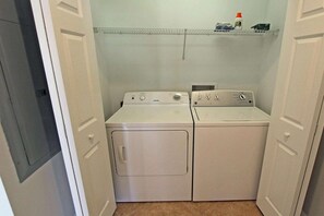 Une buanderie équipée de deux machines à laver et deux sèche-linge superposés, une étagère au-dessus pour ranger les produits de nettoyage, et une porte donnant sur une autre pièce.