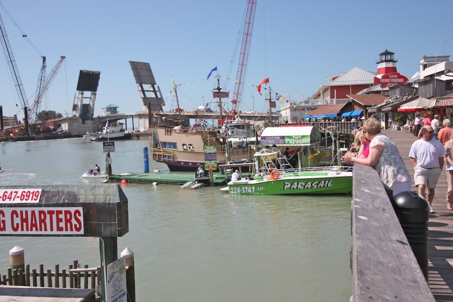 A waterfront pier with boats docked, a lighthouse, and a sign for 'Friendly Fishermen'.