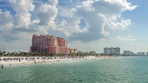 Un hotel frente a la playa con un edificio grande, una playa de arena y cielo despejado.
