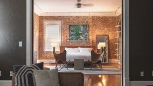 Une pièce moderne avec un mur en briques, un canapé blanc, deux fauteuils, une petite table et un ventilateur de plafond.