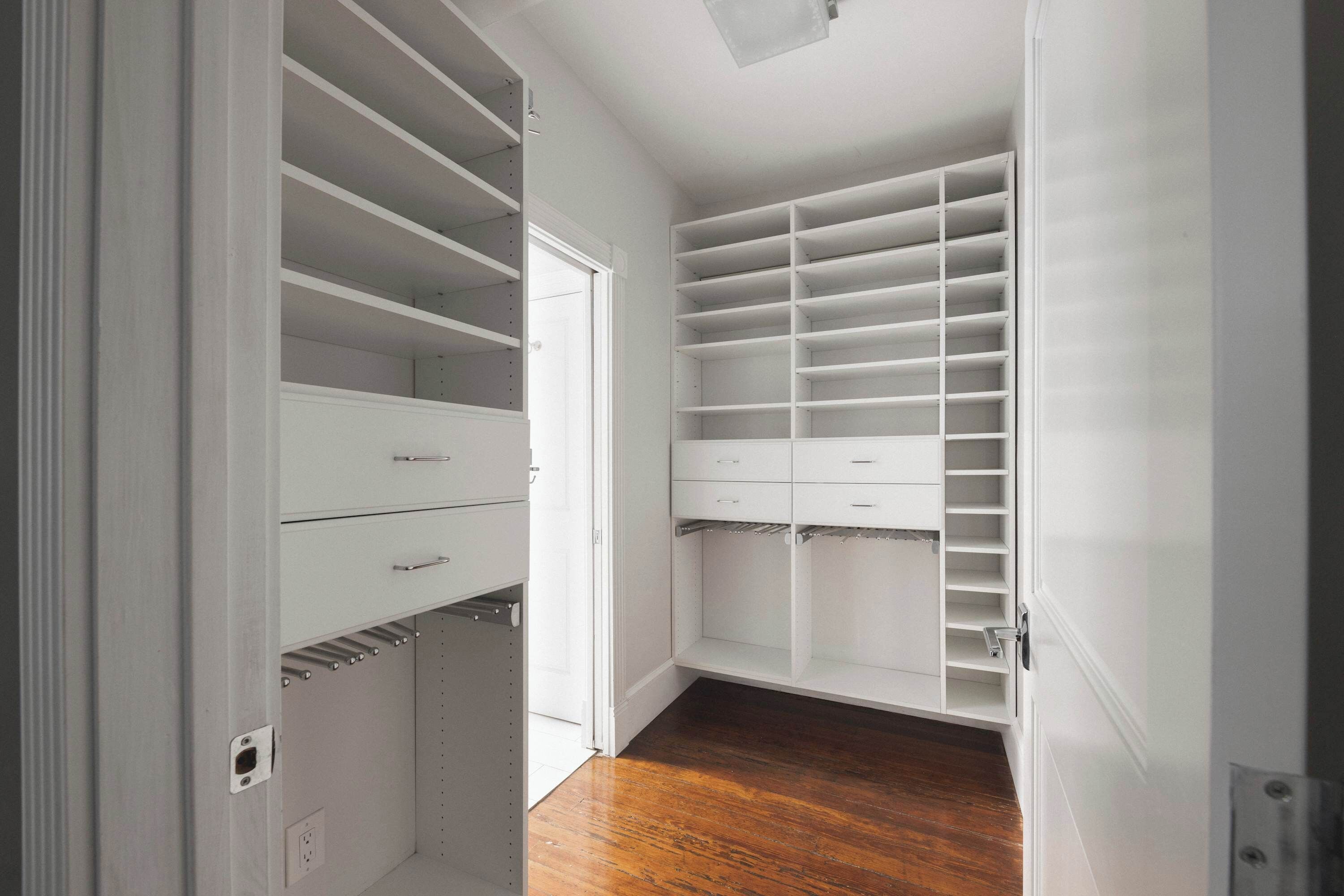 A walk-in closet with multiple shelves and drawers, a wooden floor, and a white door.