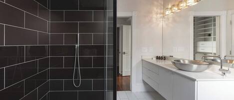 Un baño moderno con ducha envuelta en vidrio, un lavabo grande de color blanco y un espejo sobre el lavabo.