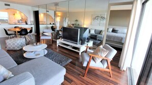 Ein modernes Wohnzimmer mit Sofa, Sesseln, Fernseher und einem Essbereich mit Stühlen und Tisch.