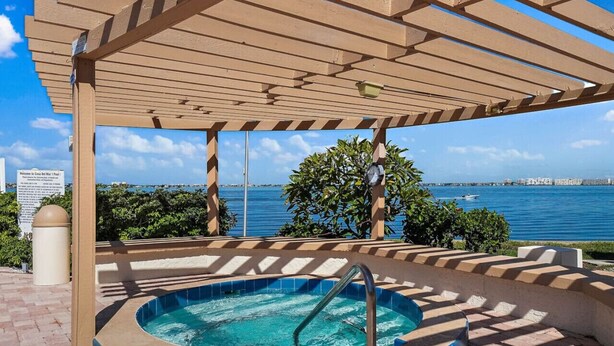 Ein Whirlpool unter einer Pergola mit Blick auf das Meer und ein Segelboot.