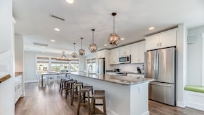 Een moderne keuken met witte kasten, roestvrijstalen apparatuur en een centraal eiland met barstoelen.