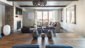 A modern living room with a wooden dining table, blue upholstered chairs, a sofa set, and a fireplace. - Easy Shuttle Access | Resort Amenities (Big Sky)