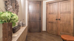 A hallway with a wooden door, a mirror, a vase with green plants, and a small table. - Easy Shuttle Access | Resort Amenities (Big Sky)
