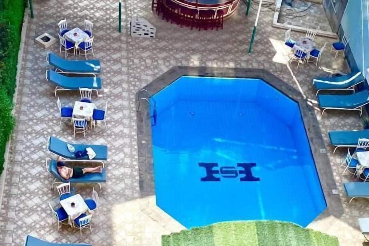 Una piscina con sillones de playa y mesas, rodeada de un patio con baldosas.