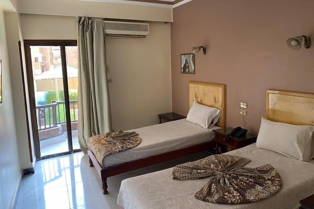 A hotel room with two beds, a balcony, an air conditioning unit, and a small table.