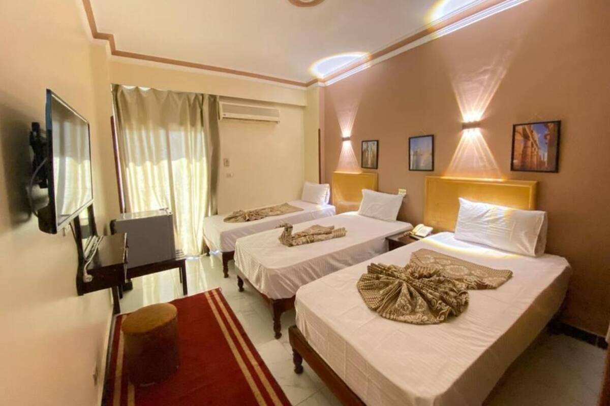 Habitación de hotel con tres camas, un escritorio, un televisor y una alfombra roja.