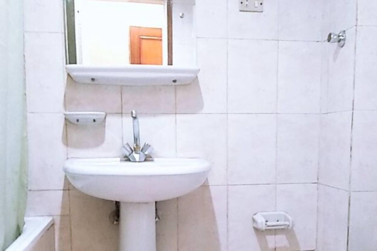 Un baño con lavamanos pedestal, un espejo encima, inodoro y un estante pequeño.