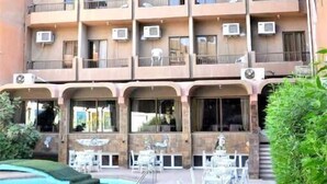 Un edificio de varios pisos con balcones, unidades de aire acondicionado y un área de piscina con mobiliario exterior.