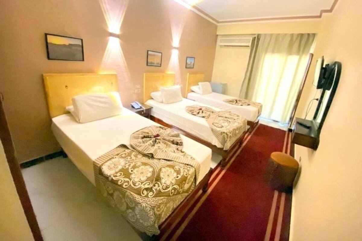 Habitación de hotel con dos camas, alfombra roja, teléfono en la pared y ventana con cortinas.