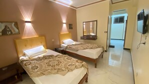 Habitación de hotel con dos camas, cada una con cabecera y mesitas de noche. Se observa un espejo en la pared y un televisor montado en la pared.