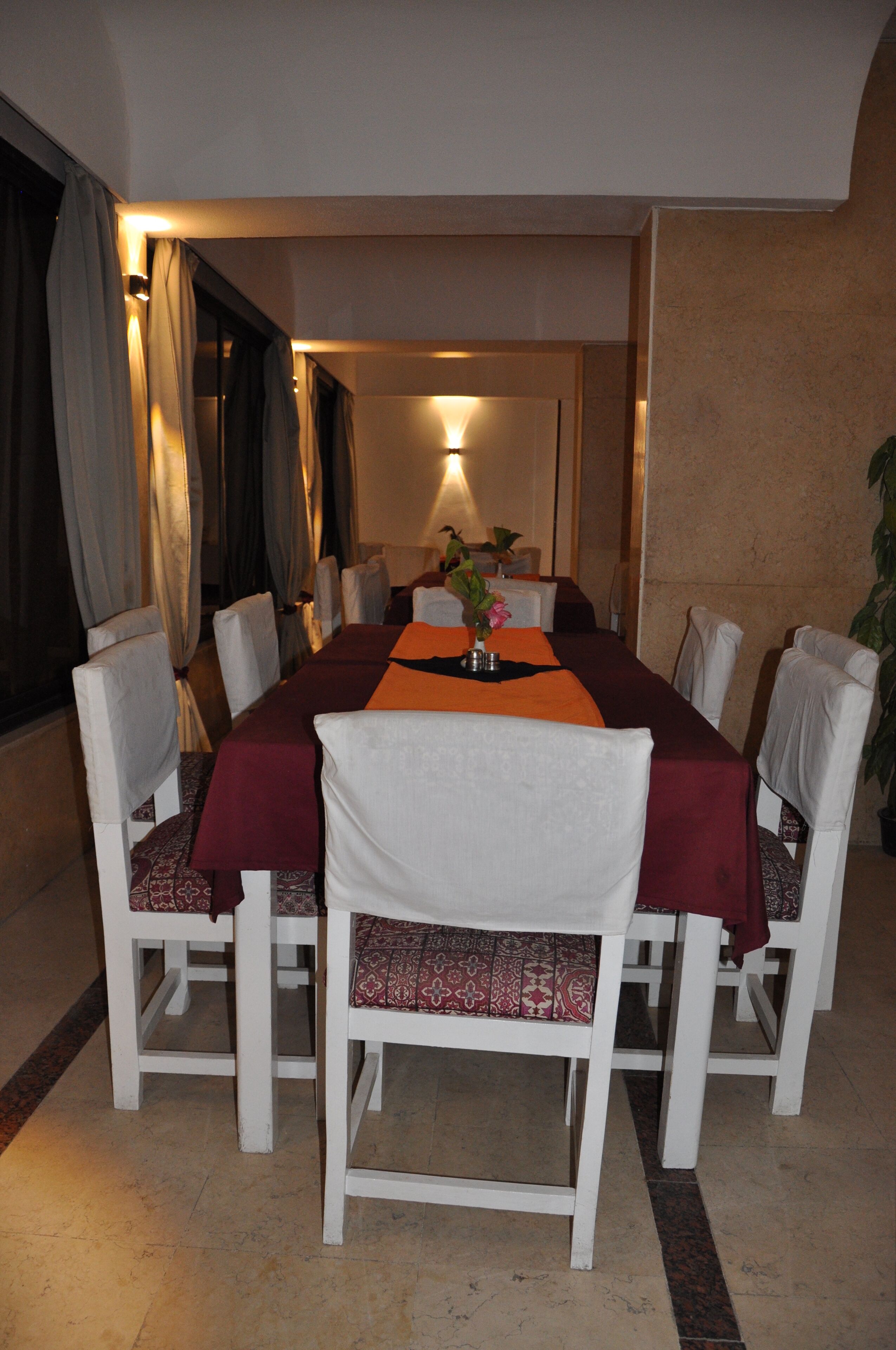 A dining area with a long table, white chairs, and a red tablecloth.