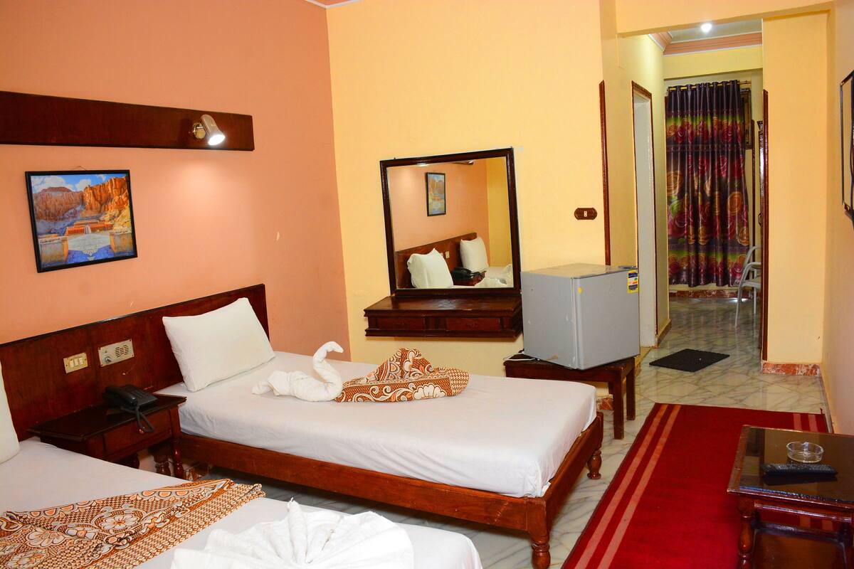 Habitación de hotel con dos camas, un escritorio, un espejo, un televisor y una alfombra roja.