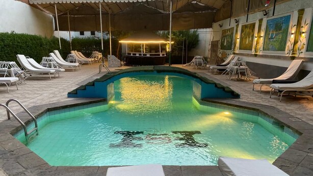 Una piscina con sillones de descanso y un área techada.