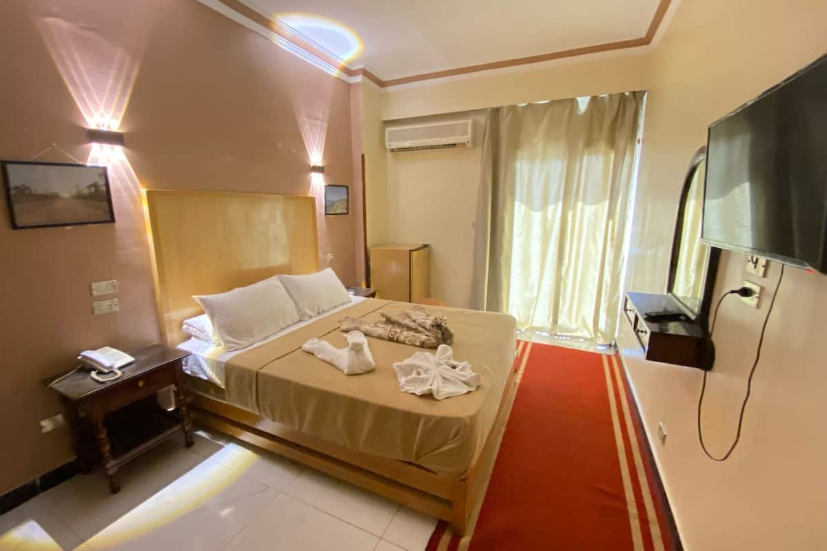 Habitación de hotel con cama, televisor, aire acondicionado, mesita de noche con teléfono y alfombra roja.