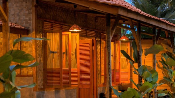 A wooden house with a tiled roof, large wooden doors, and a porch area with plants. - Cianjur Paddies Hostel (Cianjur)