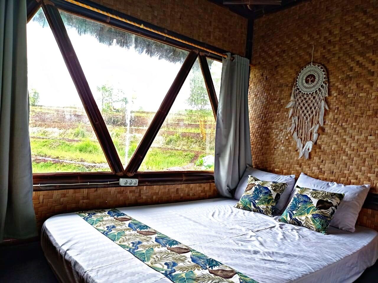 Una habitación con cama, un ventanal grande y un atrapasueños en la pared.