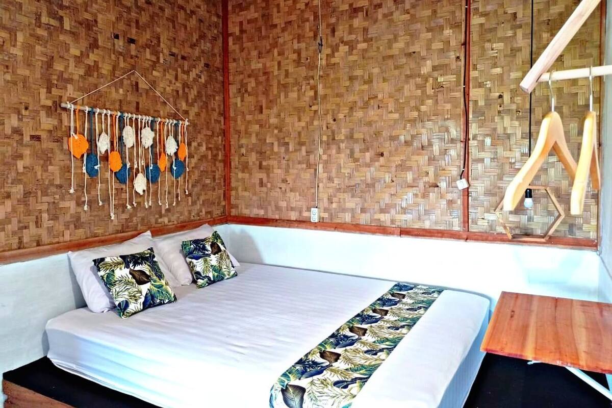 Una habitació amb un llit, una decoració penjada a la paret i una cadira de fusta.