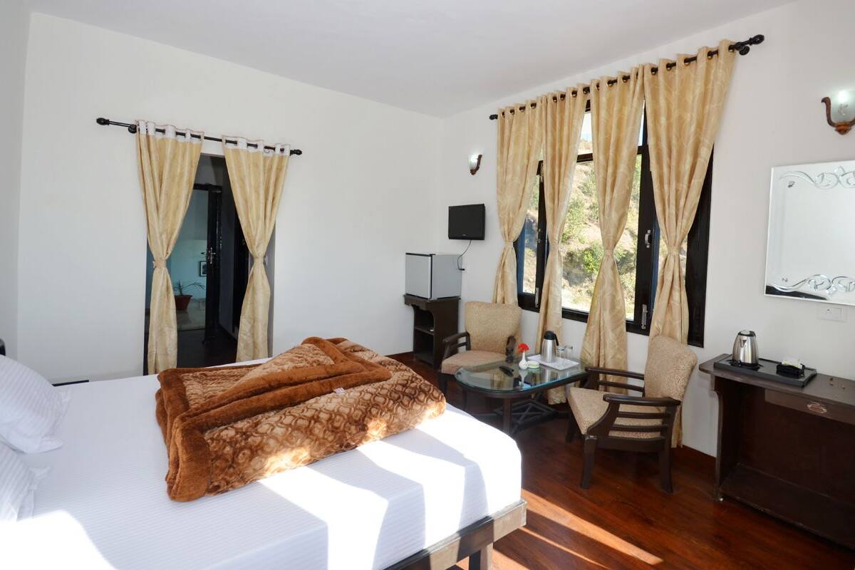 Habitación de hotel con cama, escritorio, silla, televisor y ventana con cortinas.