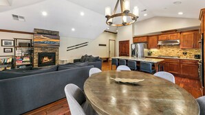 A modern living room with a fireplace, a dining area with a round table, and a kitchen with wooden cabinets and stainless steel appliances. - Luxury Mountain Retreat | Walk to Heavenly | TW504 (South Lake Tahoe)