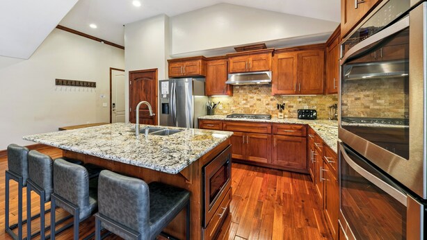A modern kitchen with wooden cabinets, stainless steel appliances, a granite countertop, and a bar area with stools. - Luxury Mountain Retreat | Walk to Heavenly | TW504 (South Lake Tahoe)