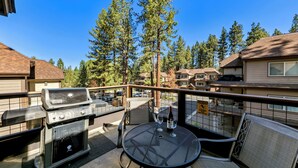 A balcony with a grill, a table with chairs, and a view of houses and trees. - Luxury Mountain Retreat | Walk to Heavenly | TW504 (South Lake Tahoe)