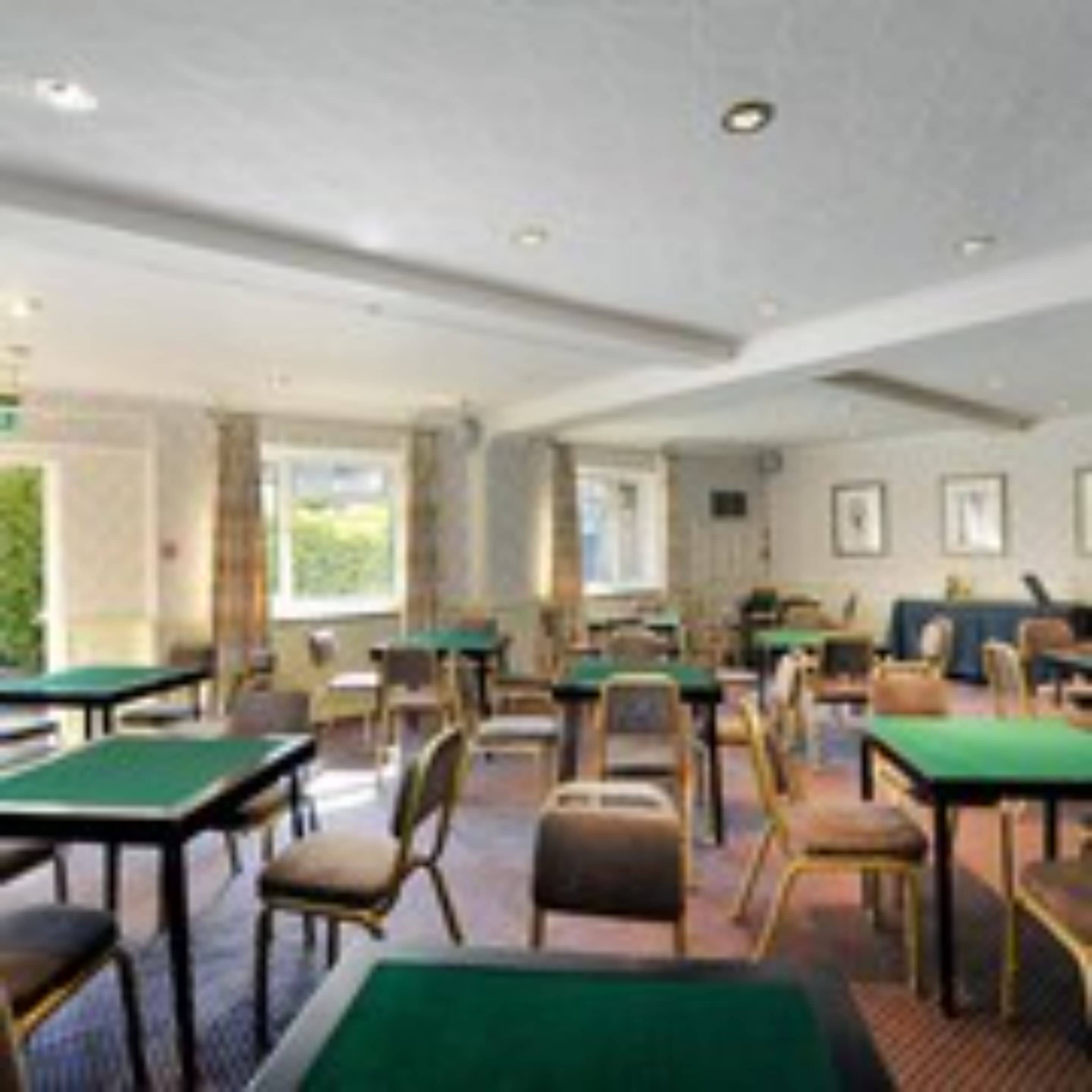 A room with multiple green pool tables and chairs, arranged in a casual layout.