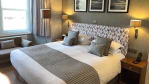 A hotel room with a large bed, two bedside tables, a window with curtains, and three framed pictures on the wall. - Ardington Hotel (Worthing)
