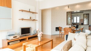 Un salon moderne avec une table basse en bois, un canapé et un téléviseur. On trouve des étagères en bois au-dessus du téléviseur, ainsi qu’un coin repas avec une table et des chaises.