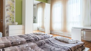 Une chambre avec deux lits, une armoire, un miroir et une fenêtre avec des rideaux légers.