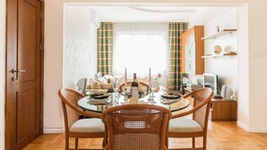 Un coin repas avec une table ronde, quatre chaises en osier, un canapé et un téléviseur en arrière-plan.
