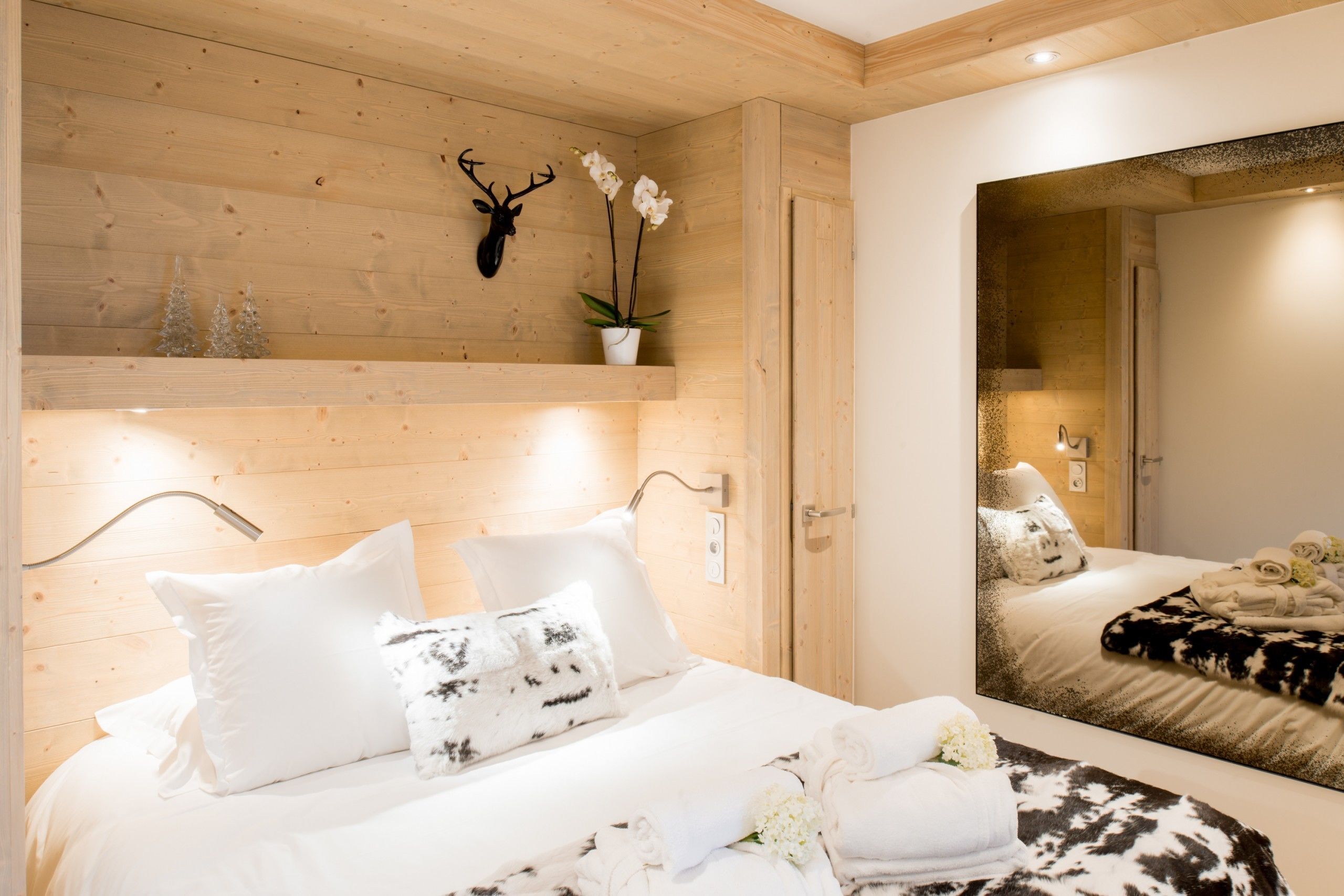 A wooden-paneled room with a bed, a mounted deer head, and a potted orchid.
