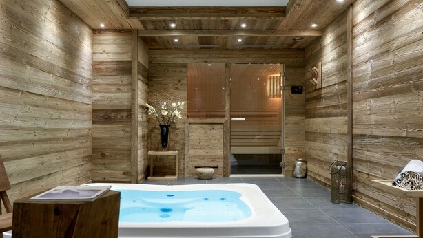 A spa room with a wooden interior, a hot tub, a small wooden table, and a vase with flowers. - Mammoth Lodge Apartment T3 Cabin D09 (Courchevel)