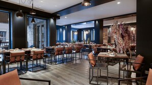 A modern restaurant interior with multiple dining tables and chairs, large windows, and hanging pendant lights. - Mammoth Lodge Apartment T3 Cabin D09 (Courchevel)