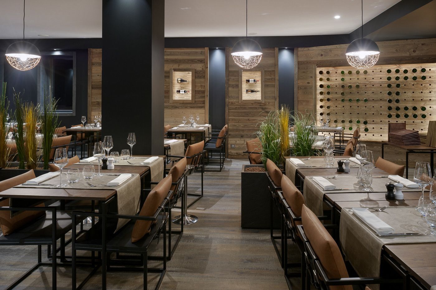 A modern restaurant with multiple dining tables, each set with wine glasses and cutlery.