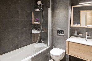 A modern bathroom with a glass-enclosed shower, a white toilet, and a wooden vanity with a mirror.