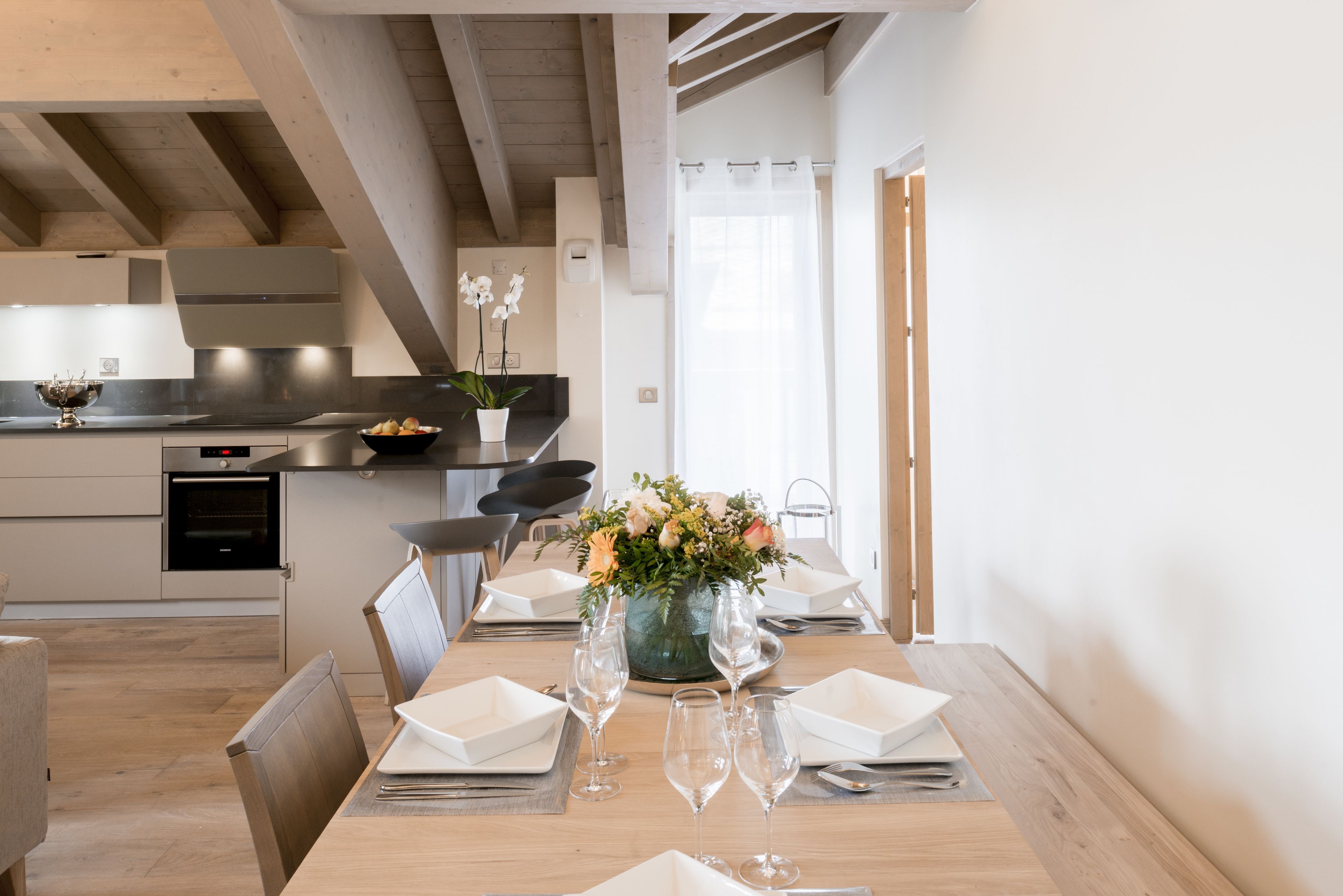 A modern kitchen with wooden beams, a dining area with a table set for four, and a vase of flowers on the table.