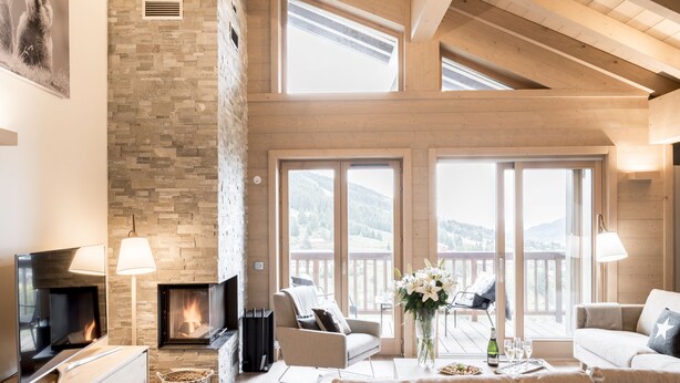 Amplia sala de estar con chimenea, ventanas grandes y un balcón con vistas a las montañas.
