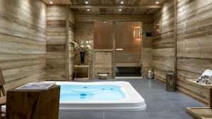 Un interior de madera con una bañera de hidromasaje, paredes de madera y una pequeña mesa con un libro.
