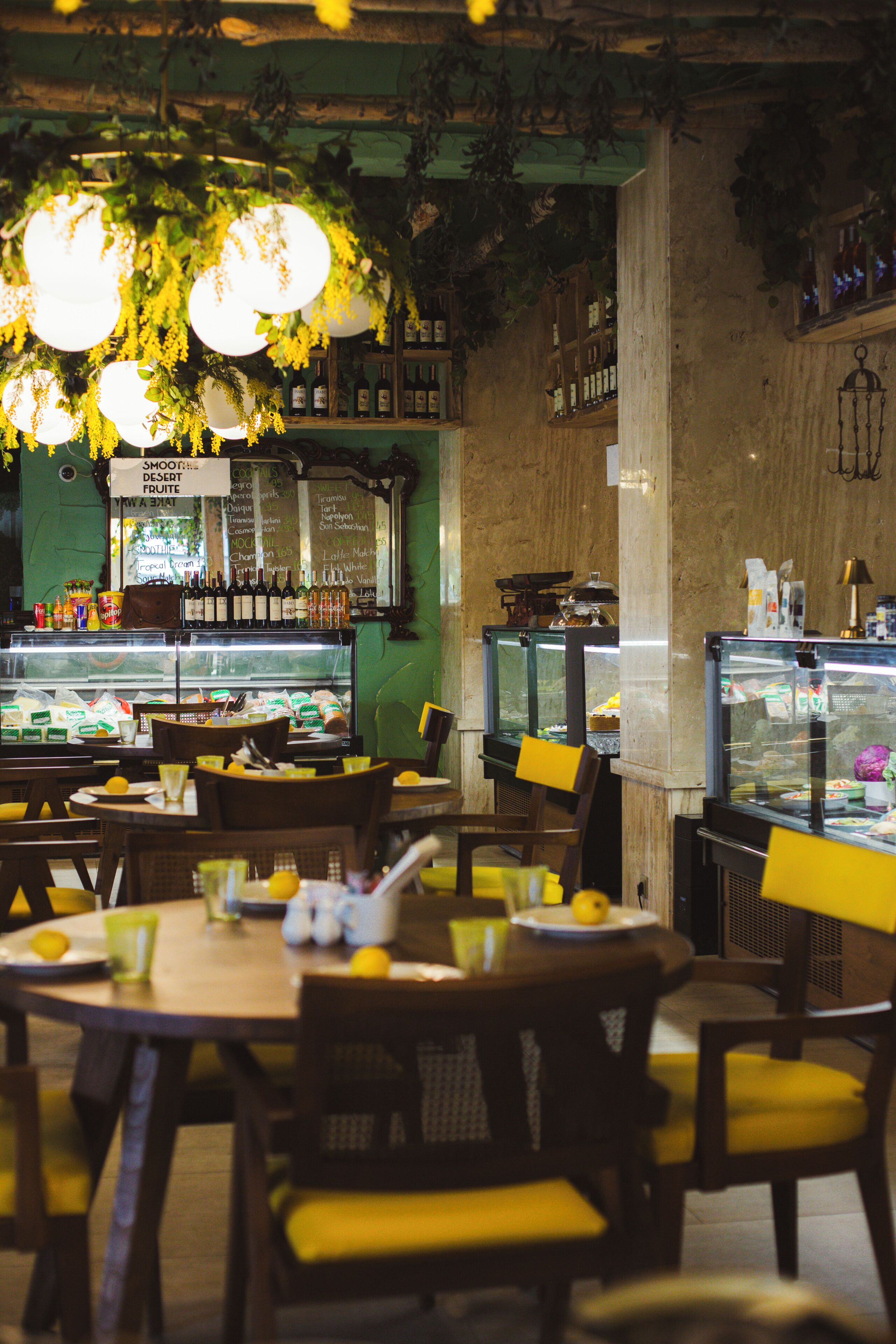 A restaurant interior with tables, chairs, hanging lights, and a display case with food items.