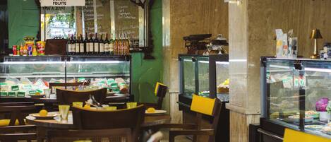 A restaurant interior with tables, chairs, hanging lights, and a display case with food items.