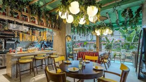 Un restaurante con zona de bar, mesas al aire libre y plantas colgantes.