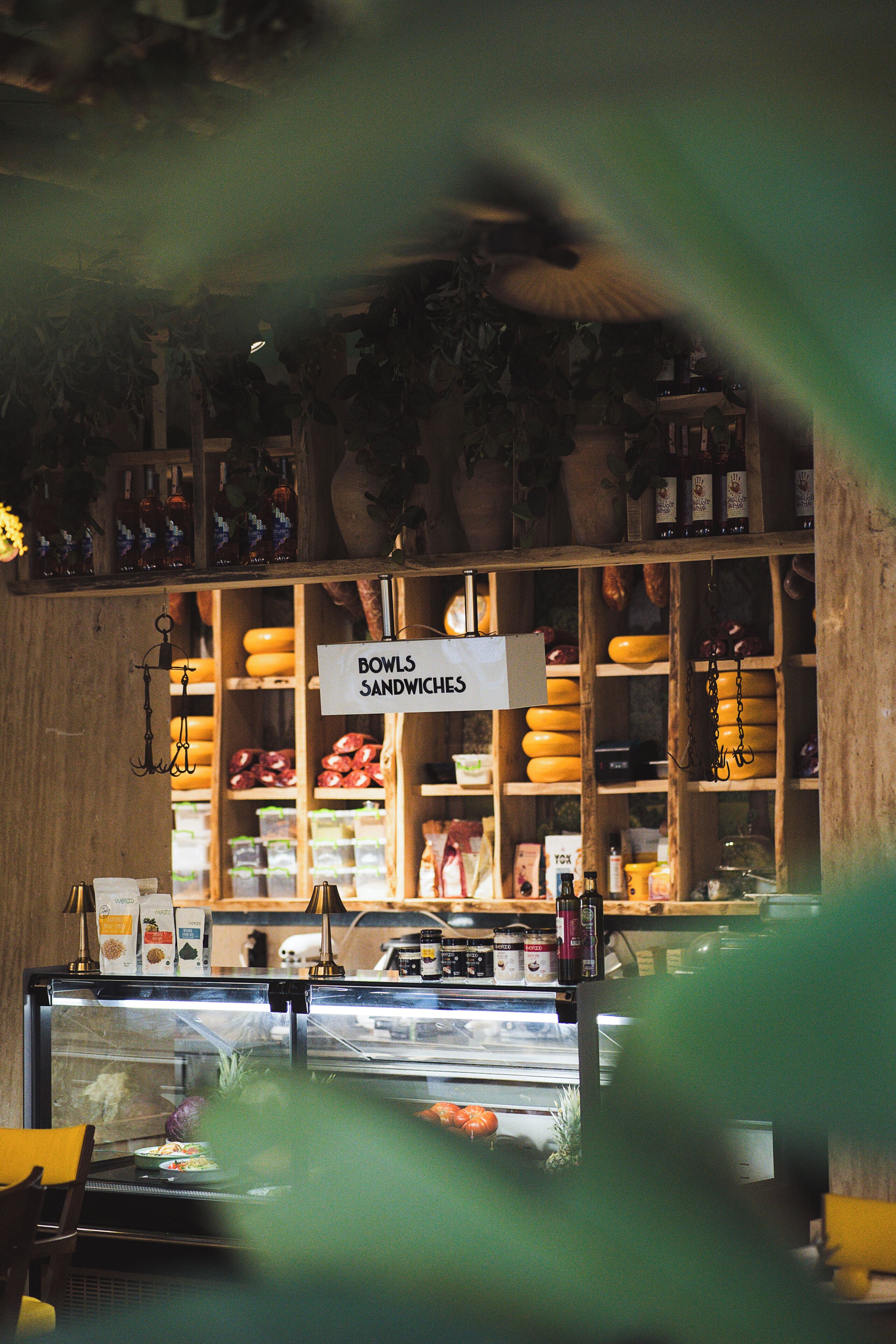 A deli counter with a sign for bowls and sandwiches, shelves with various food items, and a display case with food.