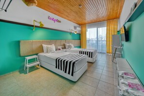 Une chambre d’hôtel avec deux lits, une petite table, un banc, une télévision et un balcon avec des rideaux jaunes.