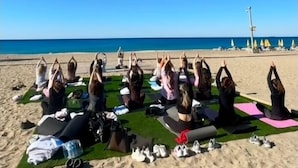 Un grupo de personas sentadas sobre esteras en la playa, mirando al mar.